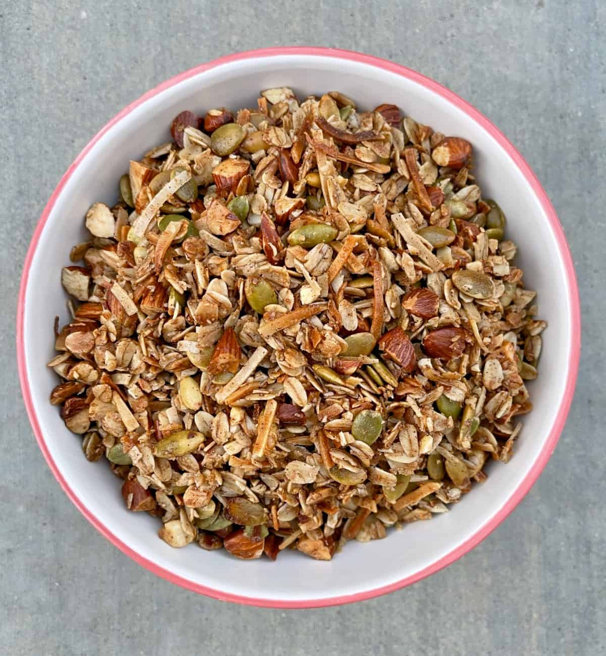 Air fryer toasted oat granola with chopped almonds and pumpkin seeds in white bowl from above.
