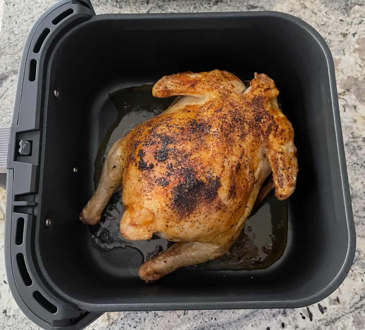Whole chicken cooking in air fryer basket with breast-side down.