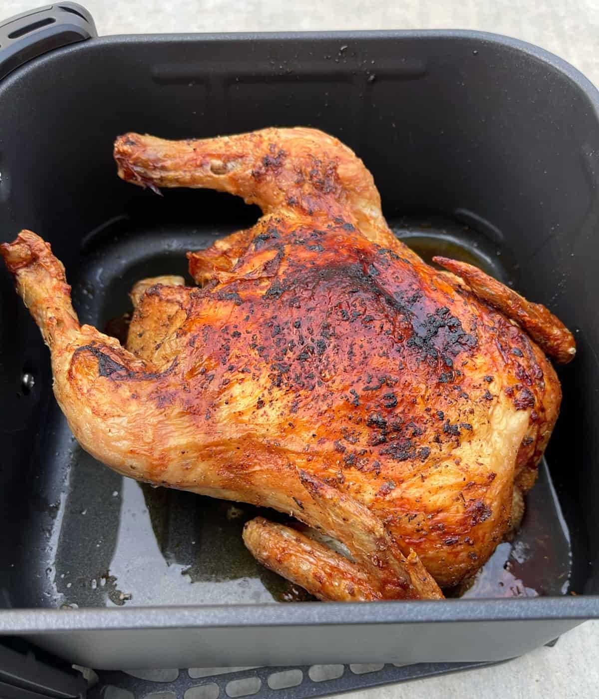 Fresh cooked air fryer roasted whole chicken in air fryer basket.