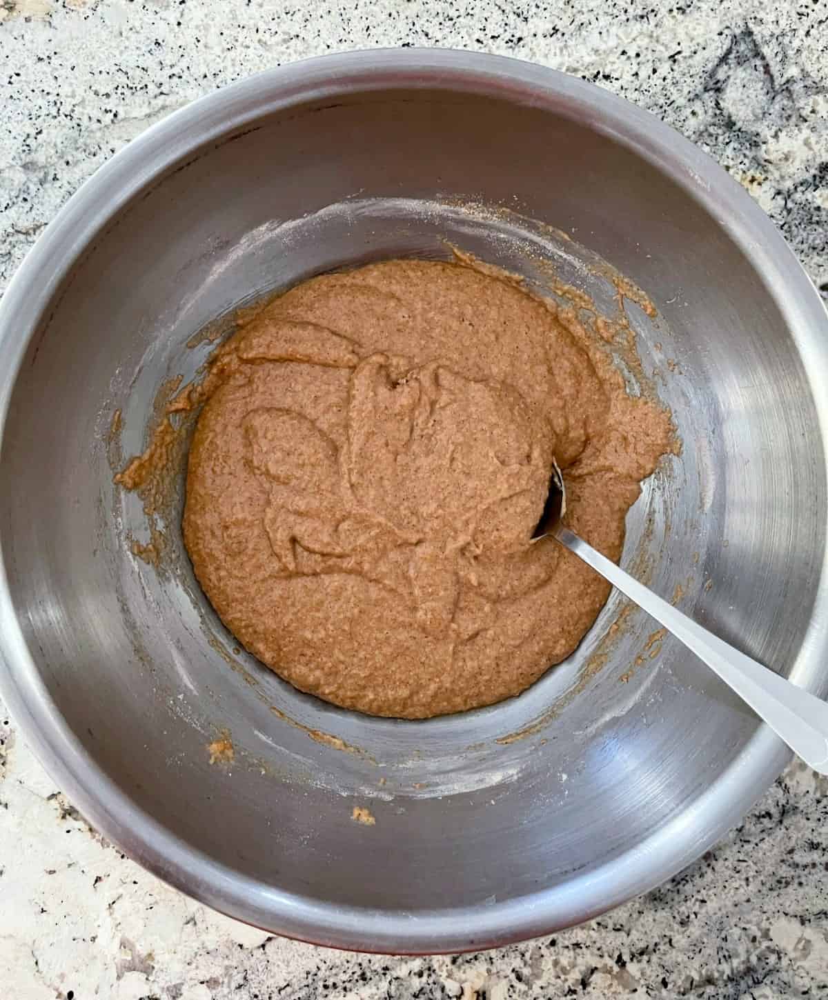 Stirring cinnamon applesauce muffin batter in mixing bowl with spoon.