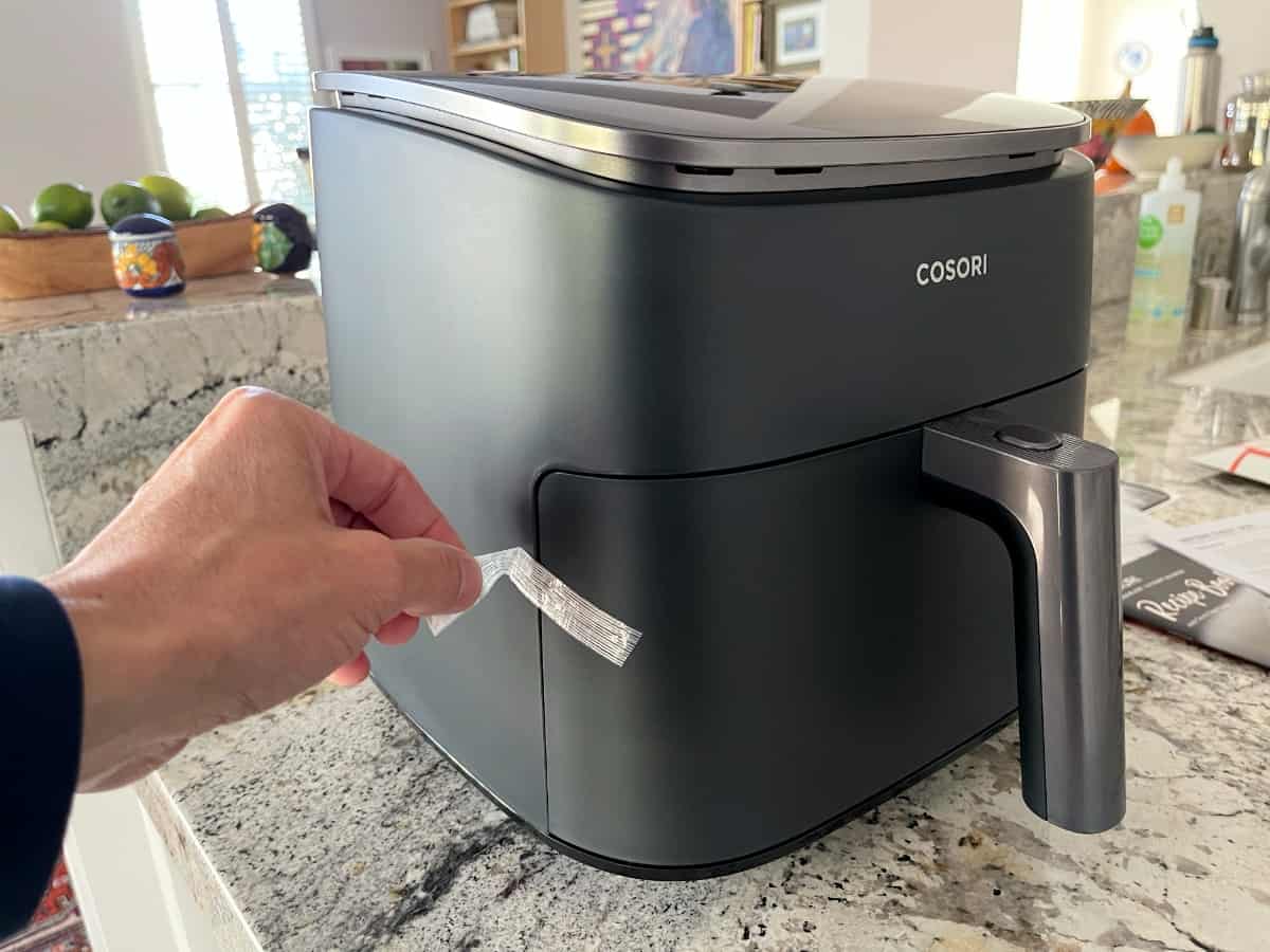 Removing the shipping tape from side of brand new Cosori air fryer holding the basket in place.