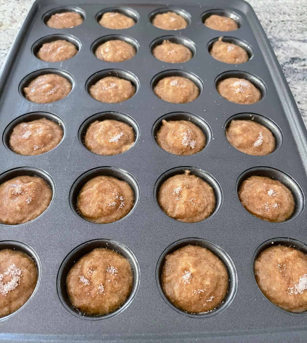 Unbaked mini cinnamon apple muffins in muffin pan with cinnamon-sugar mixture sprinkled on top.