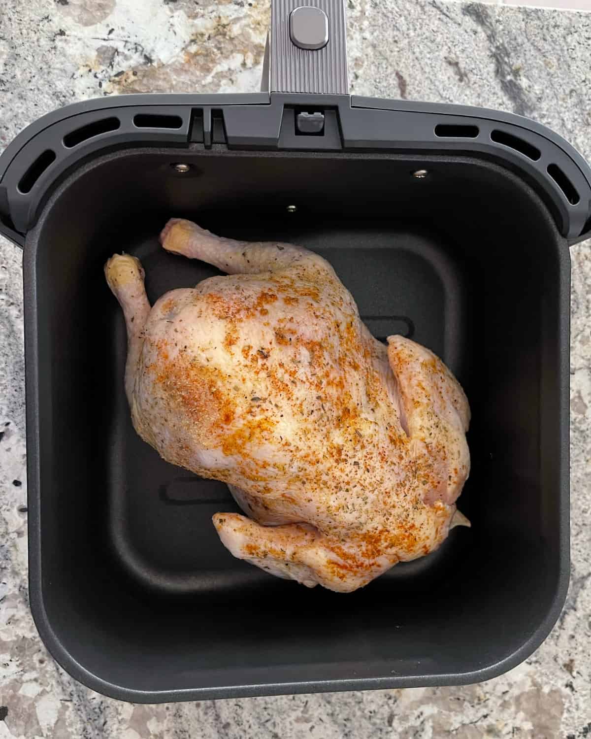 Whole seasoned chicken breast-side down in air fryer basket.