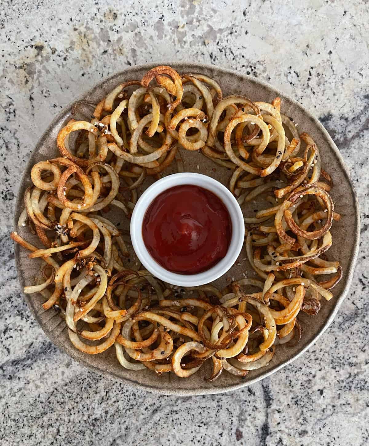 Everything bagel seasoned air fryer curly fries on plate with no sugar added ketchup.