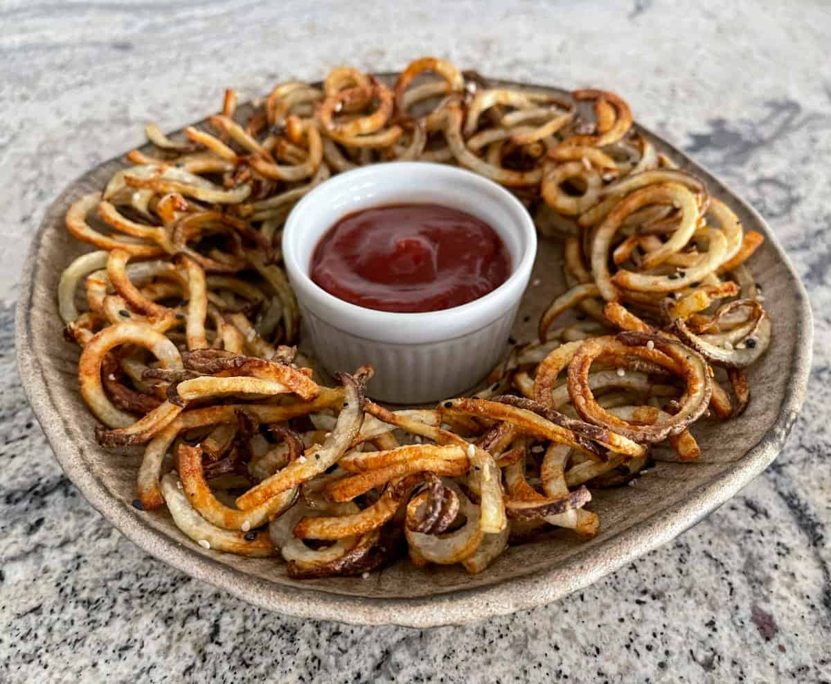 Crunchy air fryer curly fries seasoned with everything bagel seasoning on serving platter with ketchup in small white ramekin.