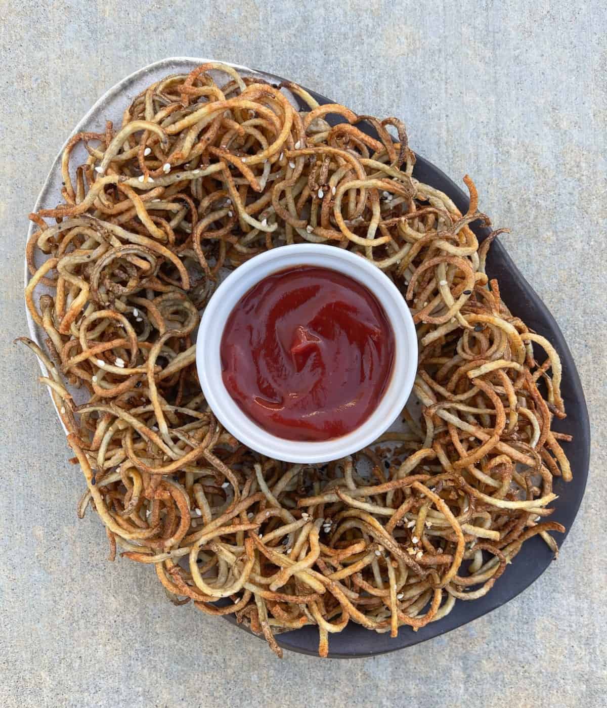 Crispy air fryer everything bagel shoestring curly fries on serving platter with ketchup.