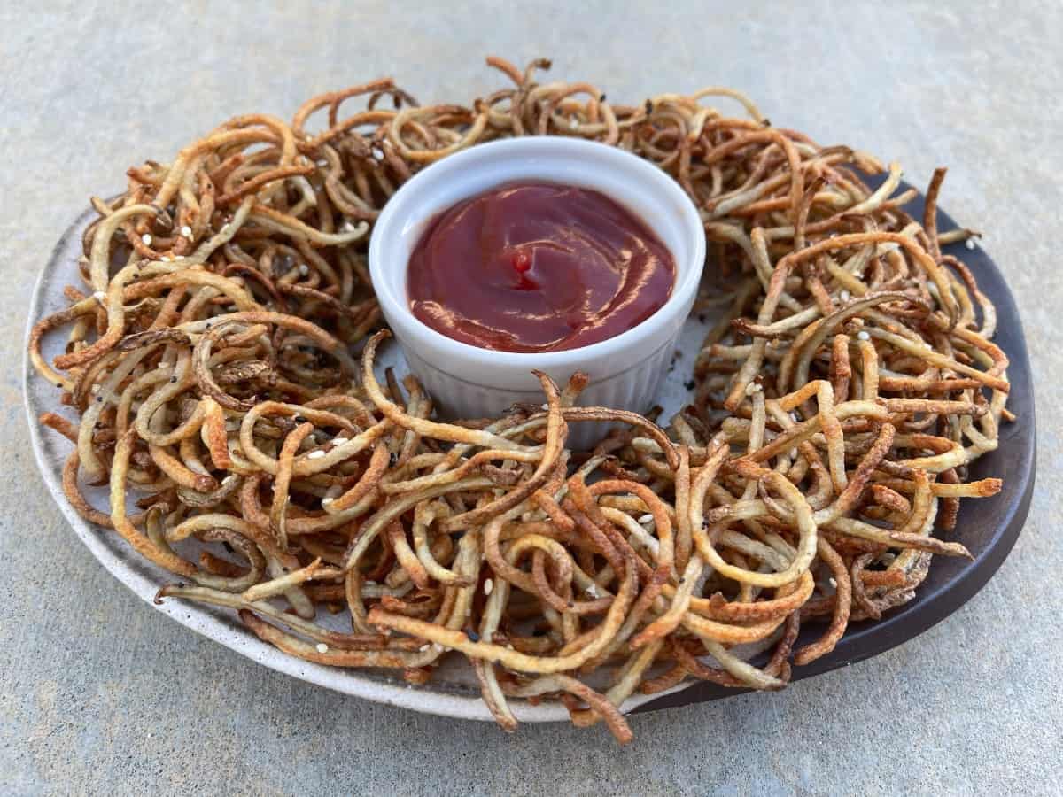 Crispy air fried shoestring curly fries with everything bagel seasoning on serving plate with ketchup.