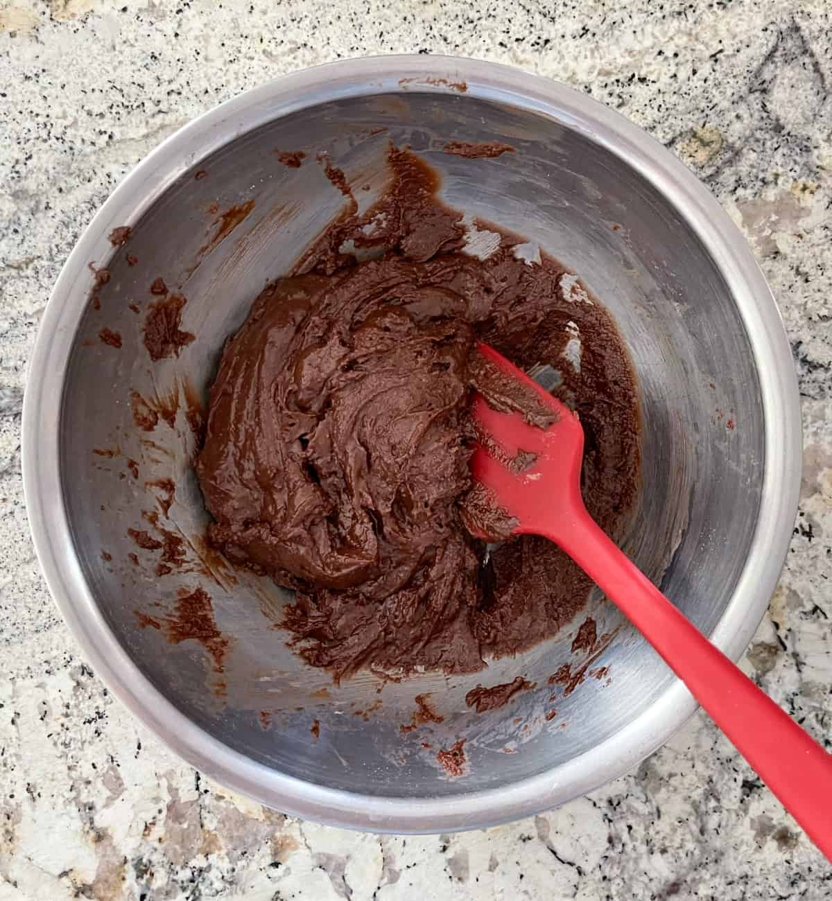 Stirring Halo Top fudge brownie mix, canola oil, water and an egg in a mixing bowl with a red spatula.