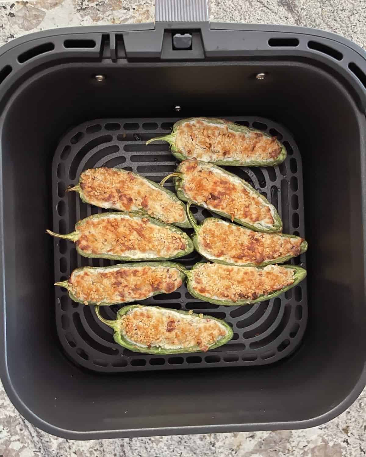 Fresh cooked jalapeno poppers in air fryer basket.