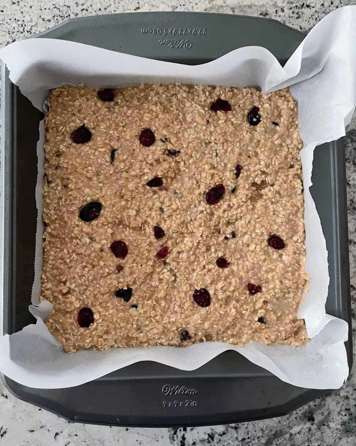 Unbaked cranberry ginger oatmeal bars in parchment lined baking pan.