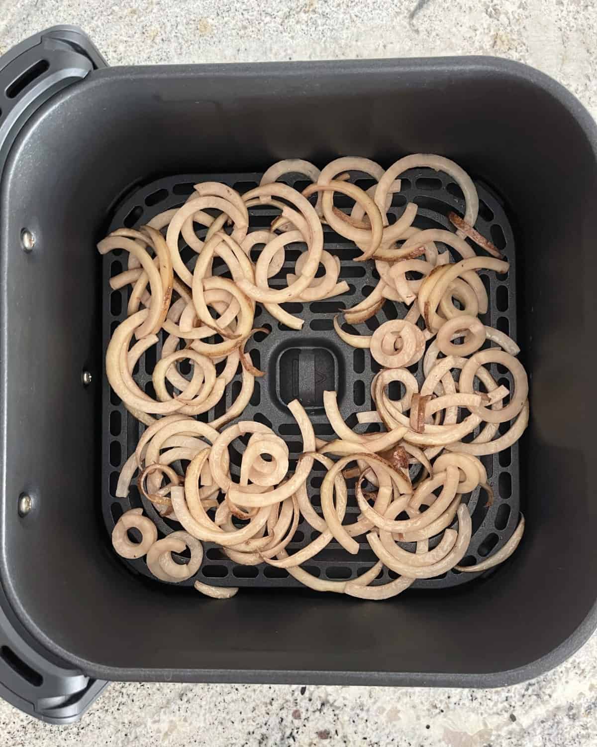 Uncooked curly fries in air fryer basket.