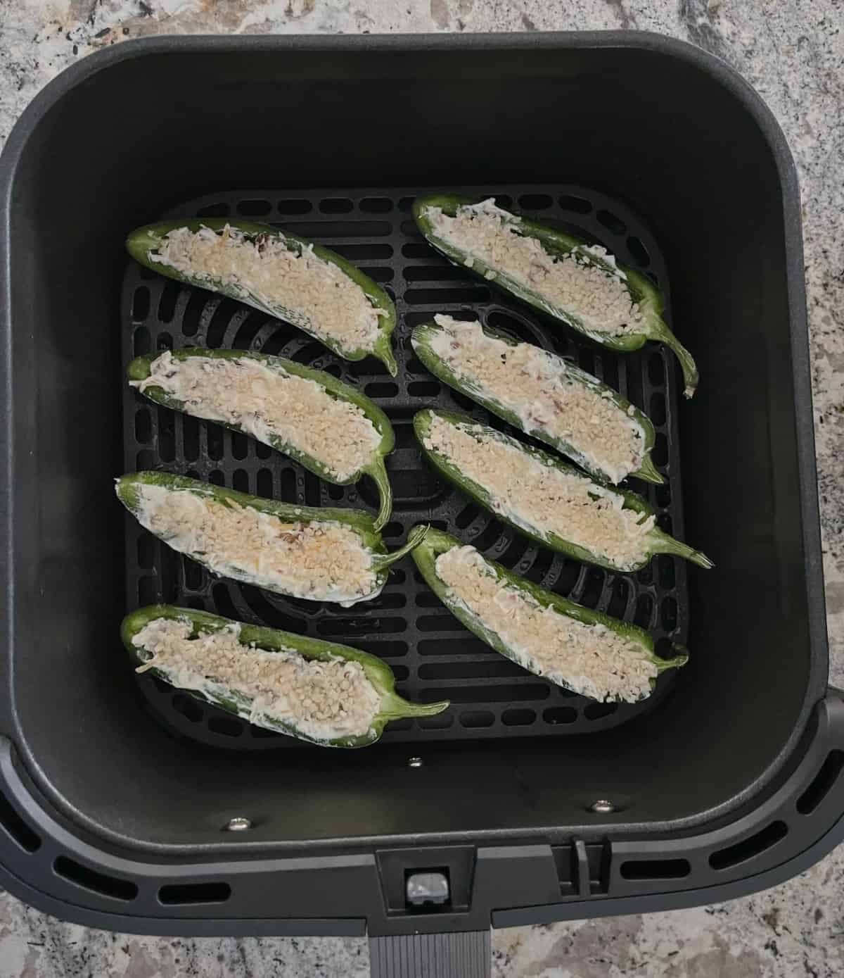 Uncooked jalapeno poppers in air fryer basket.
