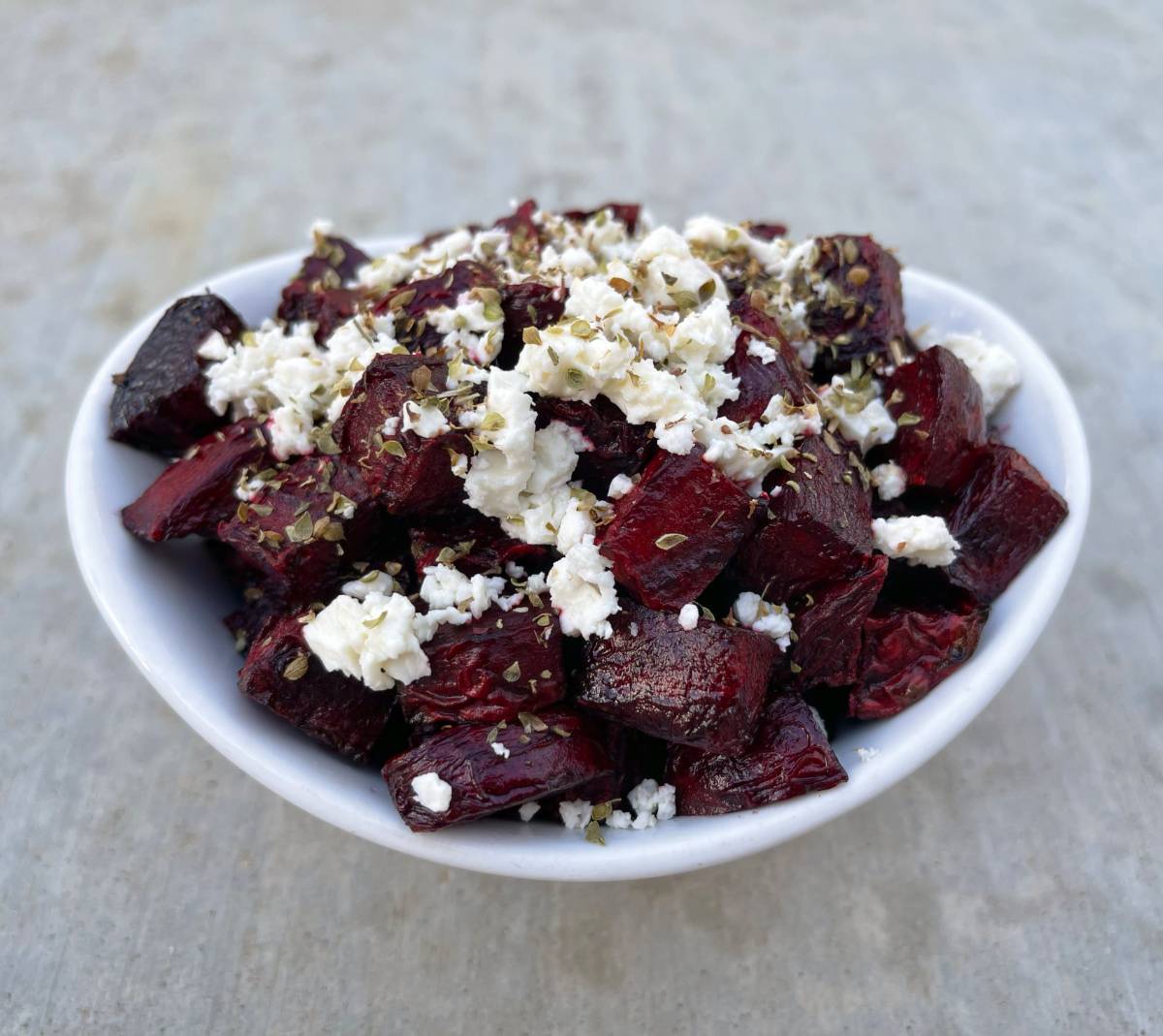 Air fryer crispy beets with crumbled feta and oregano in small white serving bowl.