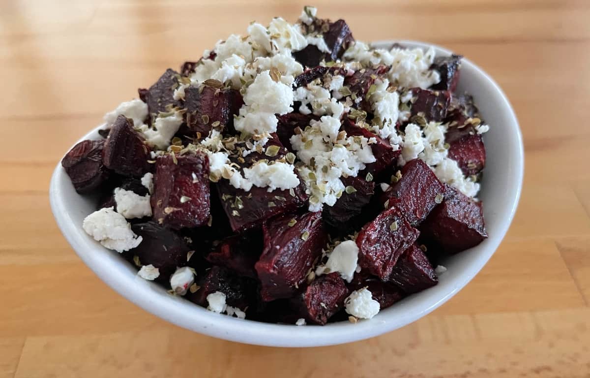Crispy beet salad with crumbled feta in small white bowl on wood table.