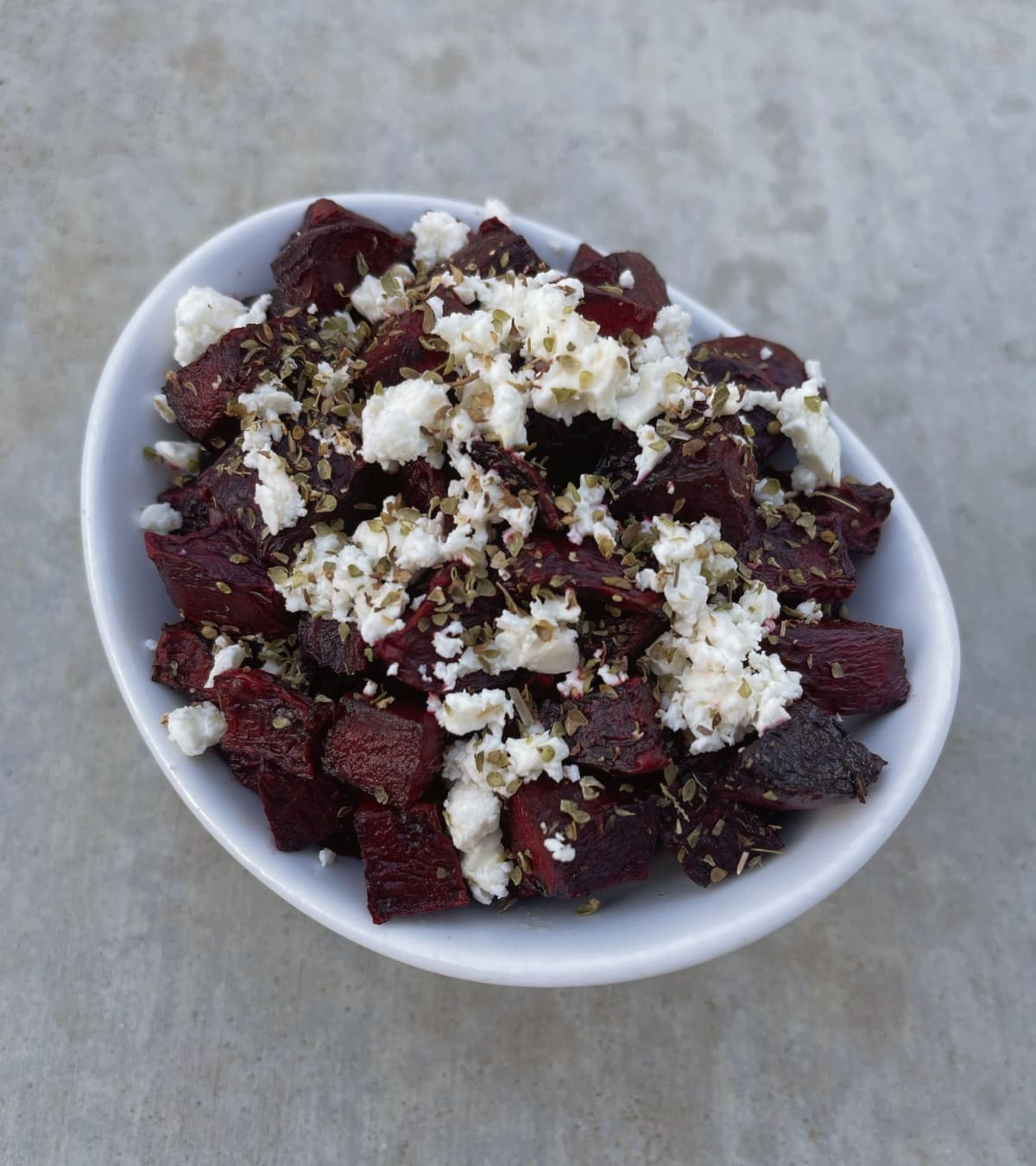 Crispy roasted beets with crumbled feta and dried oregano in white bowl.