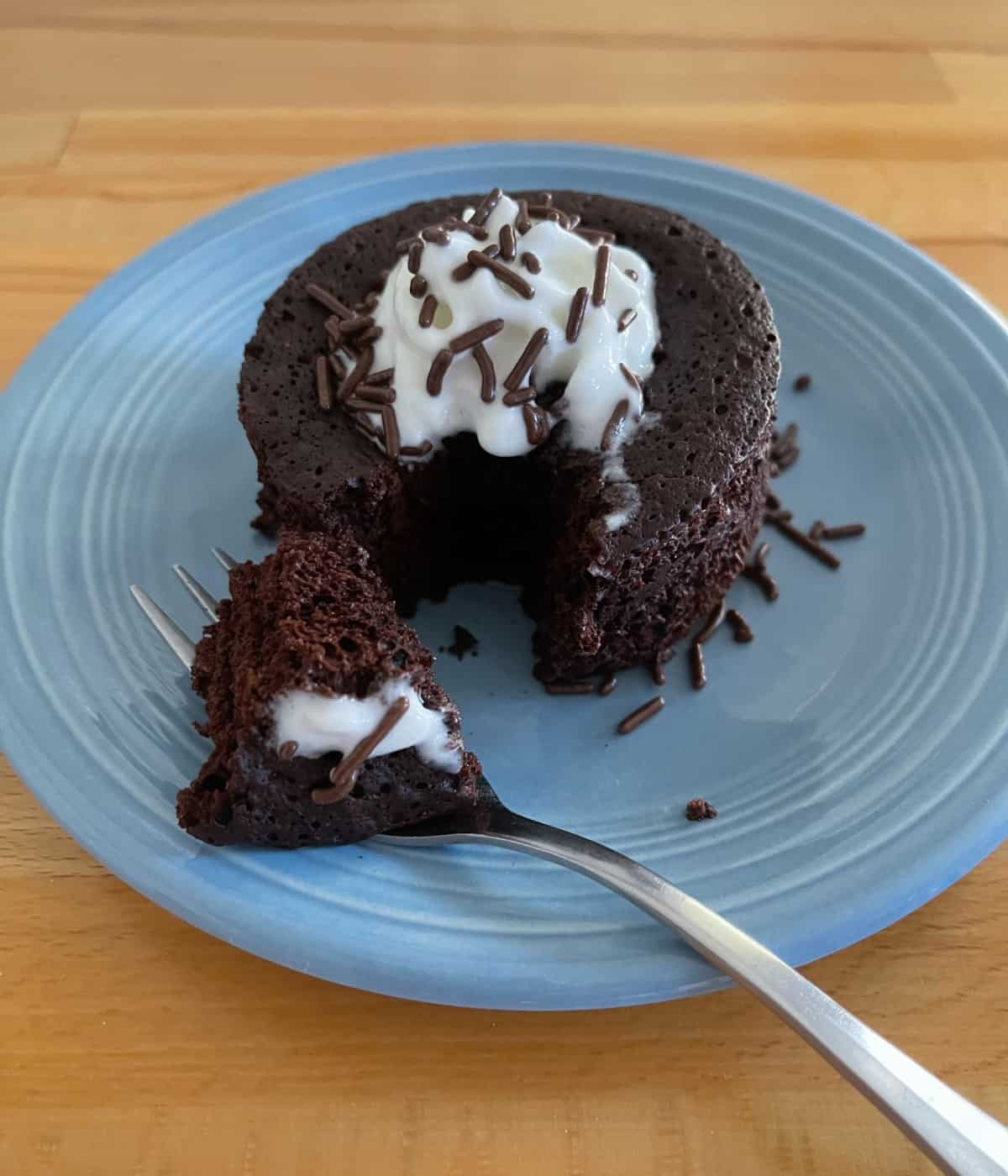 Flourless chocolate mug cake with light whipped topping and chocolate sprinkles on small blue plate with fork.