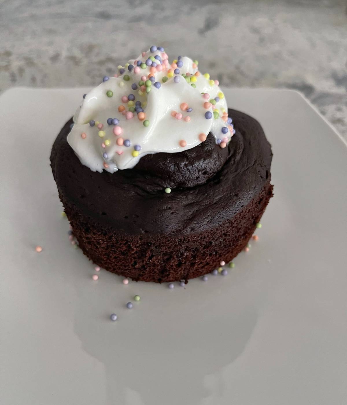 Flourless chocolate mug cake with light whipped topping and pastel sprinkles on white plate.