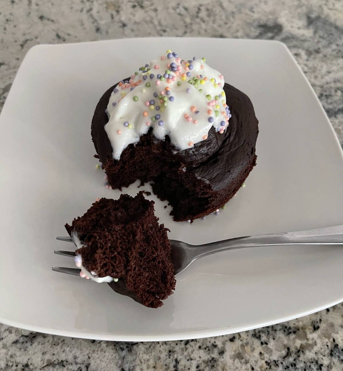 Flourless chocolate mug cake decorated with whipped topping and pastel sprinkles on small white plate with fork.