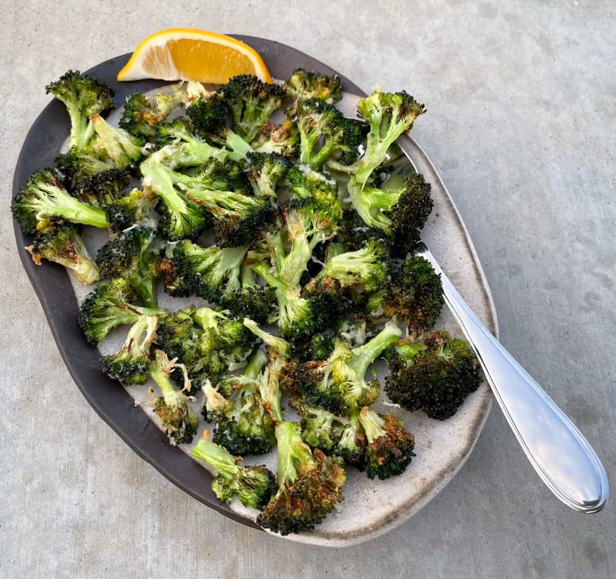Air Fried Garlic Parmesan Roasted Broccoli in serving dish with lemon wedge and spoon.
