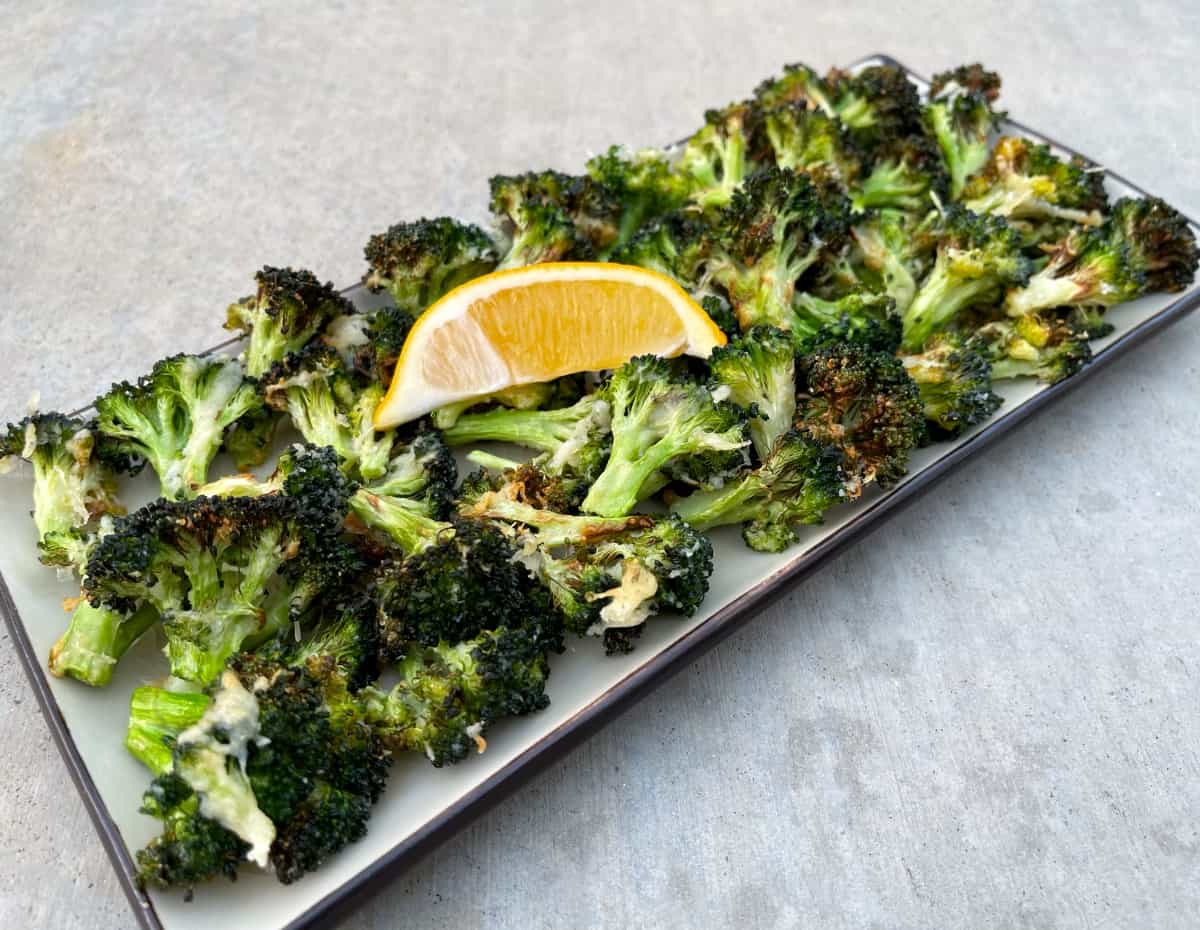 Air Fryer Roasted Garlic Parmesan Broccoli in serving dish with lemon wedge.