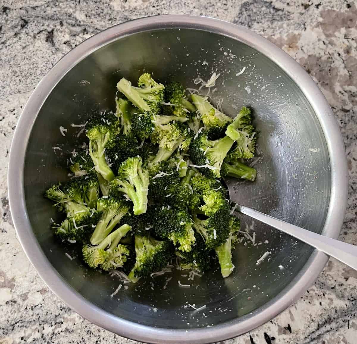 Broccoli florets, grated Parmesan, olive oil and garlic powder tossed in bowl with spoon.