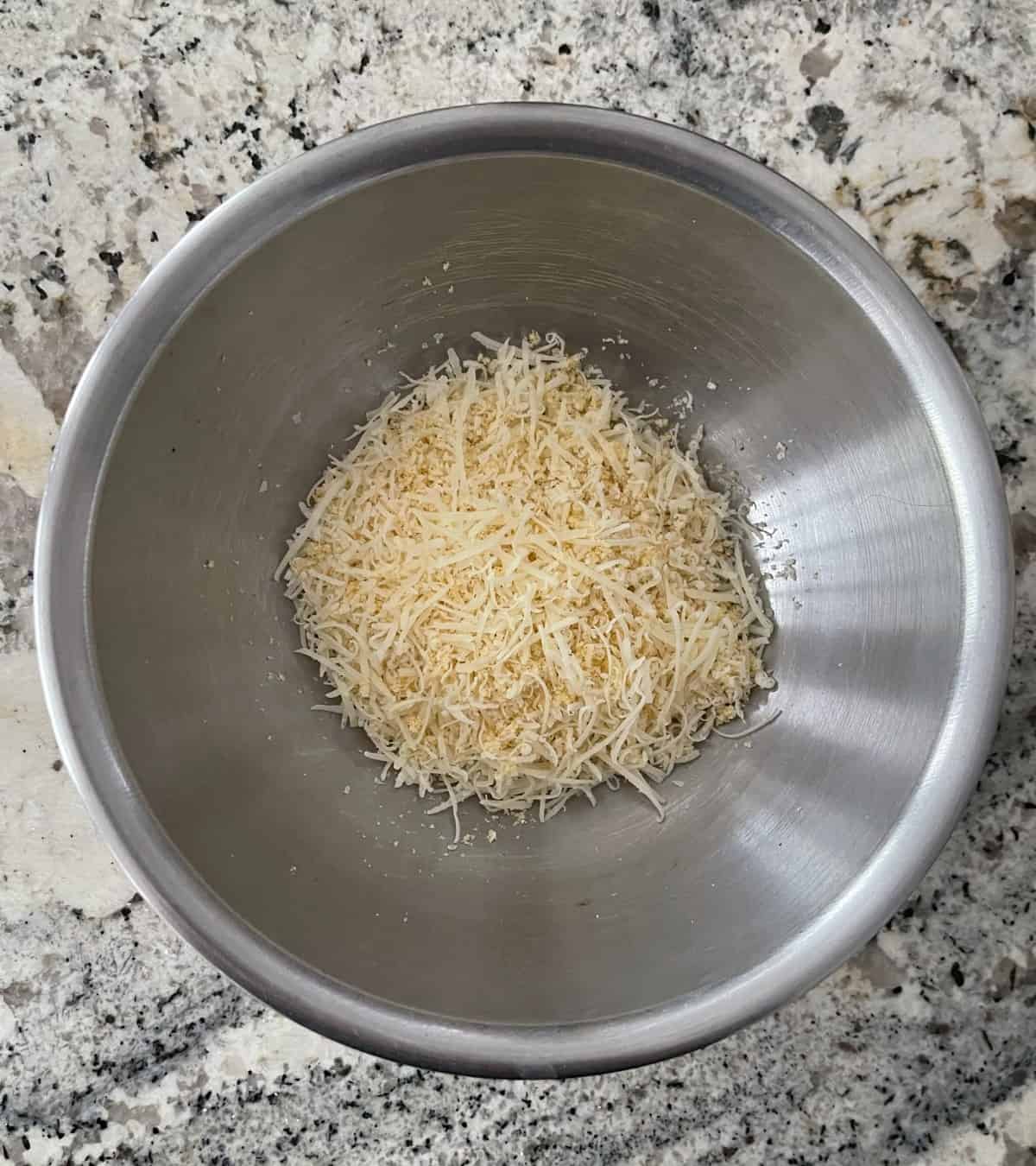 Grated Parmesan cheese mixed with onion powder, garlic powder, salt and pepper in stainless mixing bowl on granite.