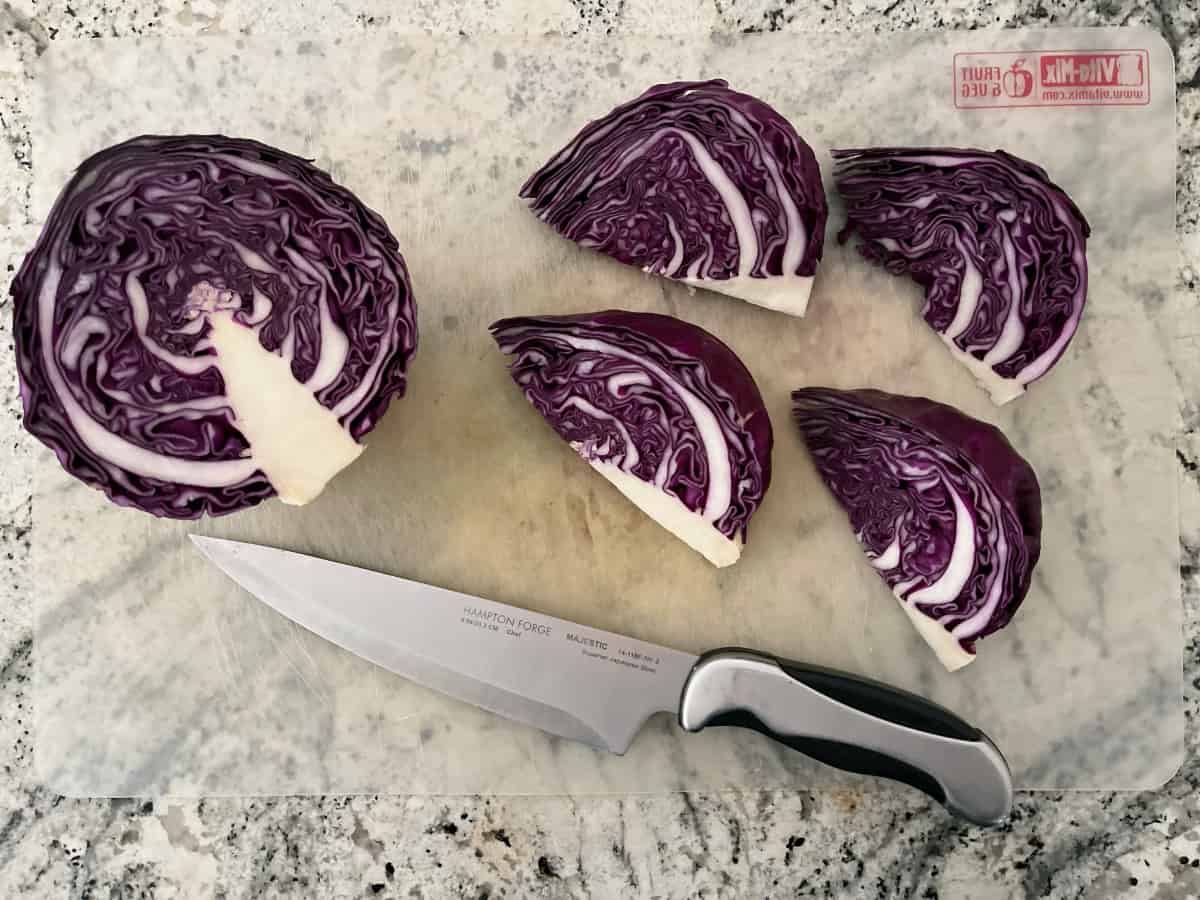 Half head of red cabbage cut into four wedges on cutting mat with chefs knife.