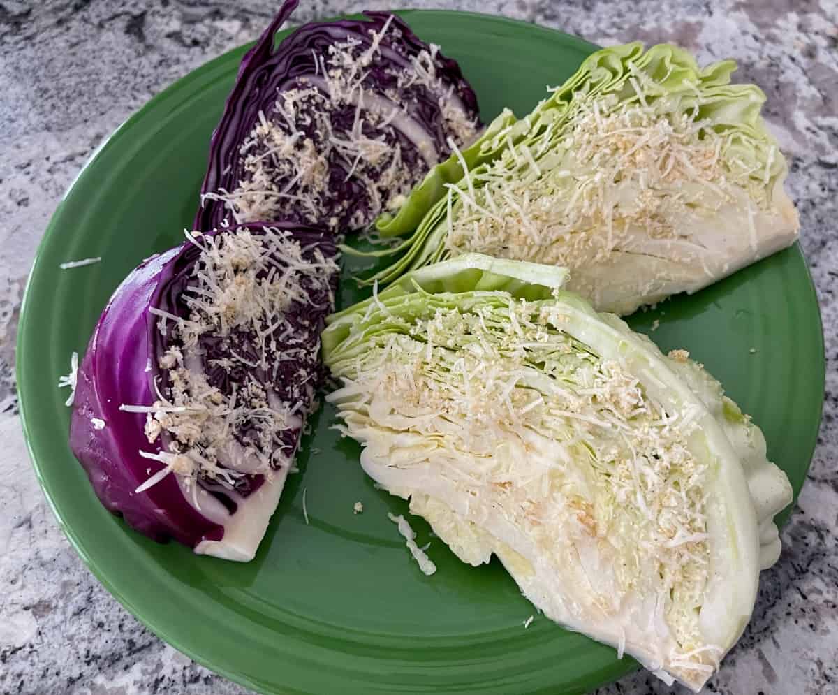 Two green cabbage wedges and two red cabbage wedges coated with olive oil, grated Parmesan cheese, garlic powder, salt and pepper on large green.