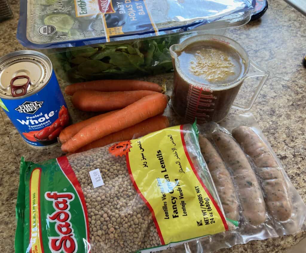 Ingredients for Slow Cooker Lentils with Sausage on the Counter: Fresh baby spinach, Cooked Chicken & Spinach Sausage, Chicken Broth, Carrots, Canned Diced Tomatoes, Lentils