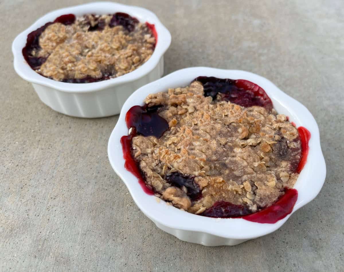 Two white ramekins with cherry berry crumble crunch dessert without topping.