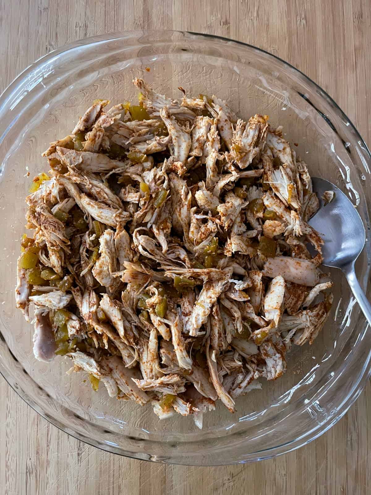 Mixing shredded chicken, chopped green chiles and taco seasoning in glass pie dish.