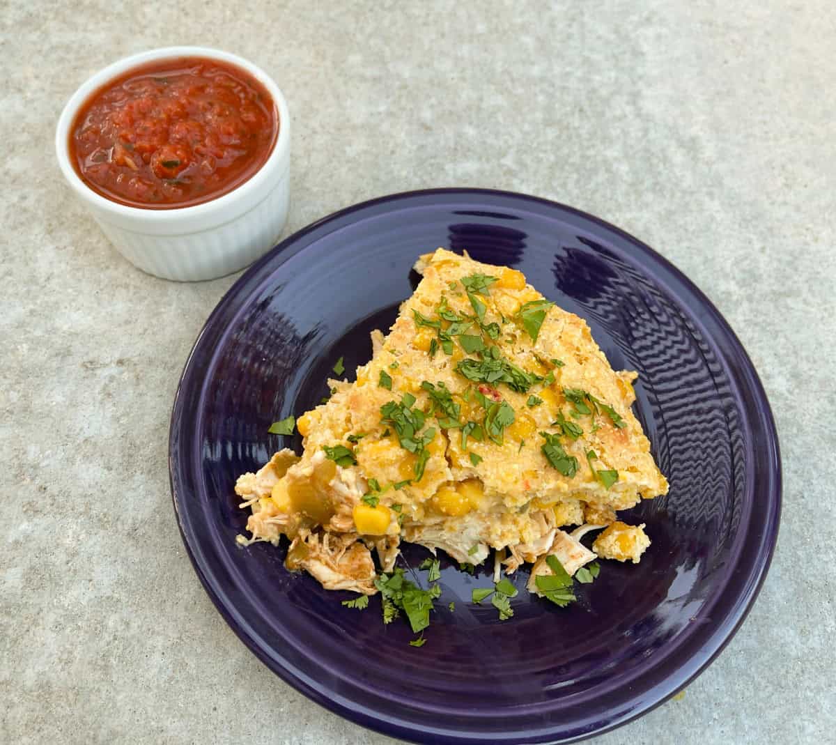 Wedge of chicken tamale pie on small plate with side of salsa in white ramekin.