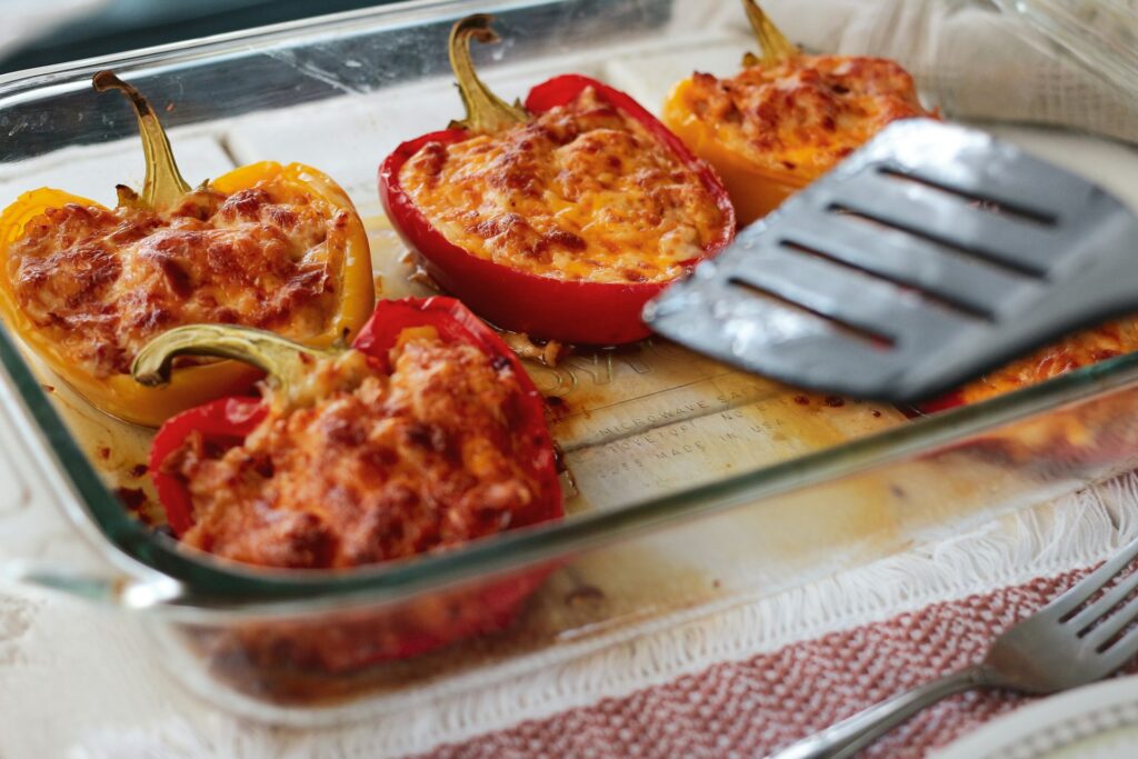 Clear glass baking dish with stuffed red bell pepper halves.