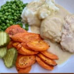 creamy crockpot chicken with carrots, peas, mashed potatoes and pickles on white plate with text box overlay