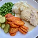 crock pot chicken cooked in creamy soup with peas, roasted carrots and pickles on white plate