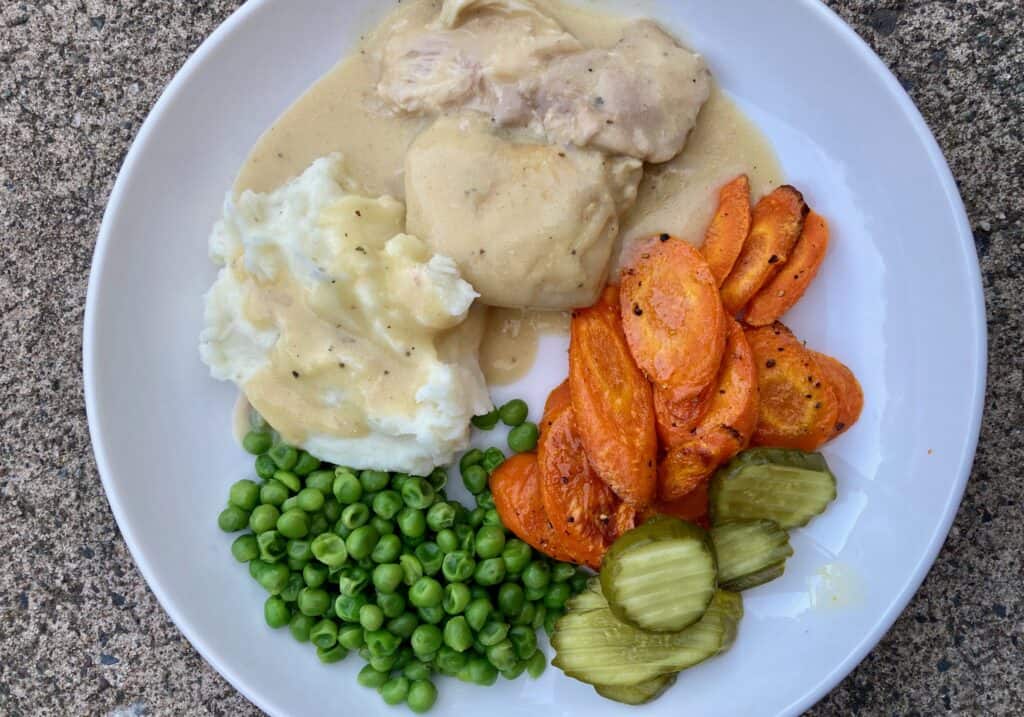 plate with creamy crock pot chicken, mashed potatoes, roasted carrots, peas, pickles