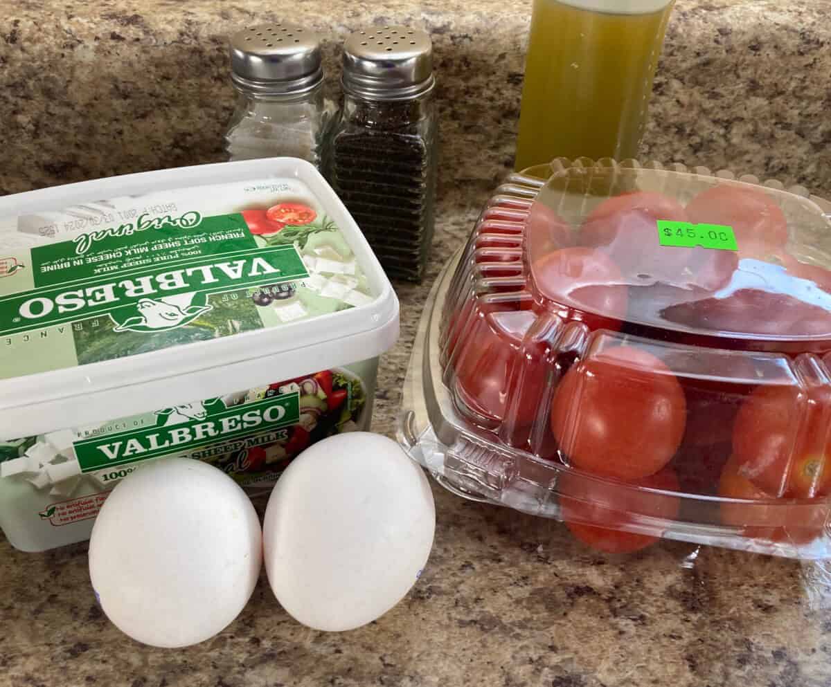 2 large white eggs, box of cherry tomatoes, carton of feta cheese, bottle of olive oil, salt and pepper on counter.