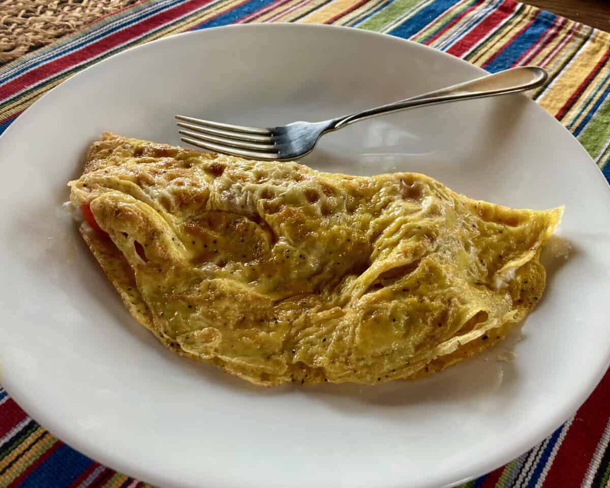 Crepe style omelet on white plate set on colorful striped placemat.