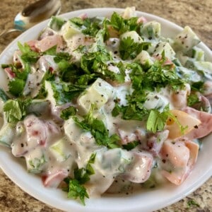 Easy Creamy Cucumber Tomatoes in Yogurt garnished with chopped fresh parsley in white serving dish on brown granite counter
