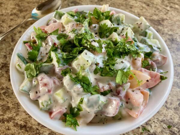 Easy Creamy Cucumber Tomatoes in Yogurt garnished with chopped fresh parsley in white serving dish on brown granite counter
