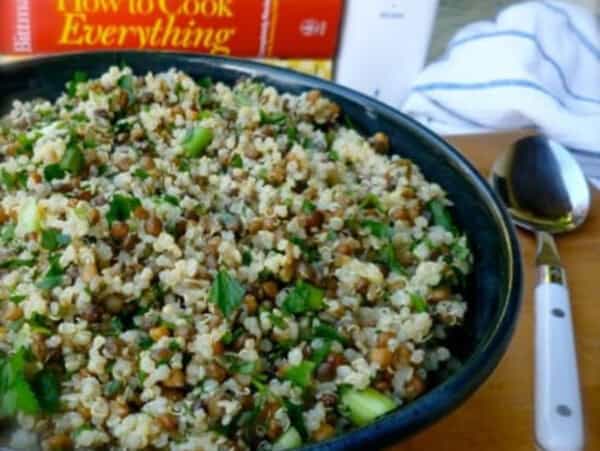 lemony lentil quinoa salad in dark blue pottery bowl with spoon alongside and cookbooks behind