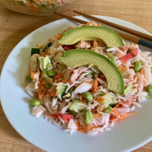 serving of sushi rice salad garnished with slices of avocado on white plate with chopsticks