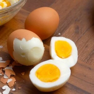 1 peeled hard boiled egg cut in half with 2 partially peeled eggs behind on counter