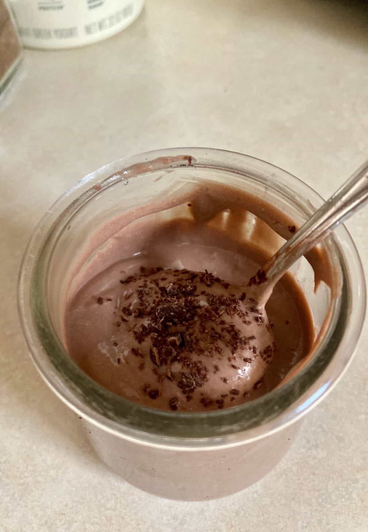 Homemade creamy Chocolate Mocha Greek Yogurt topped with chocolate shavings in a glass jar with a spoon.