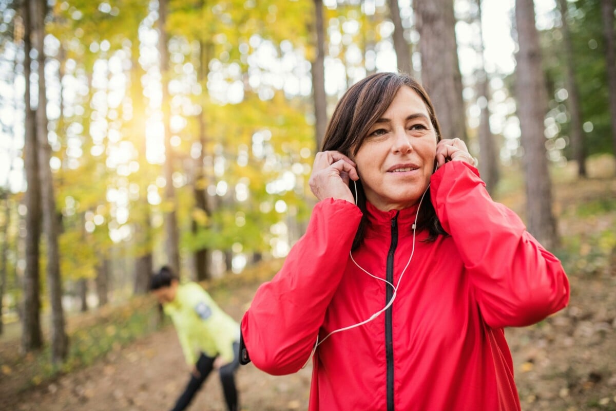 Woman in woods wearing red jacket and headphones.