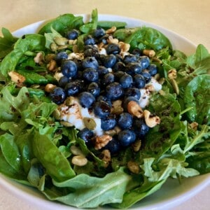 spinach salad with cottage cheese and blueberries in shallow white ceramic bowl