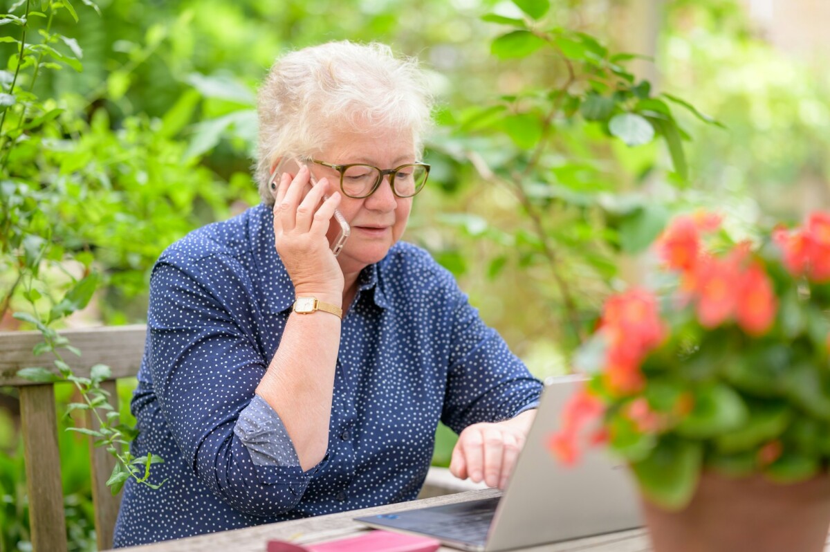 older woman talking on a cell phone with laptop in front of her