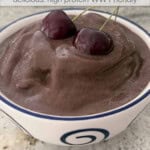 chocolate cherry smoothie bowl topped with 2 cherries in white ceramic bowl on granite counter for Pinterest PIN