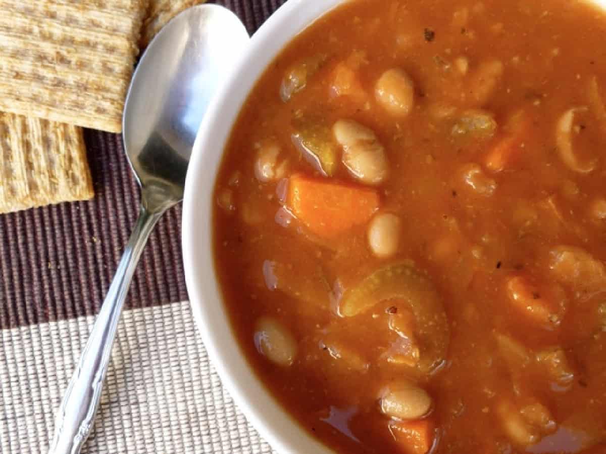 White bowl filled with bean and cabbage soup with a spoon and a few triscuits alongside.