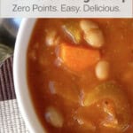 close up of white bowl of bean cabbage soup with spoon and Triscuits alongside